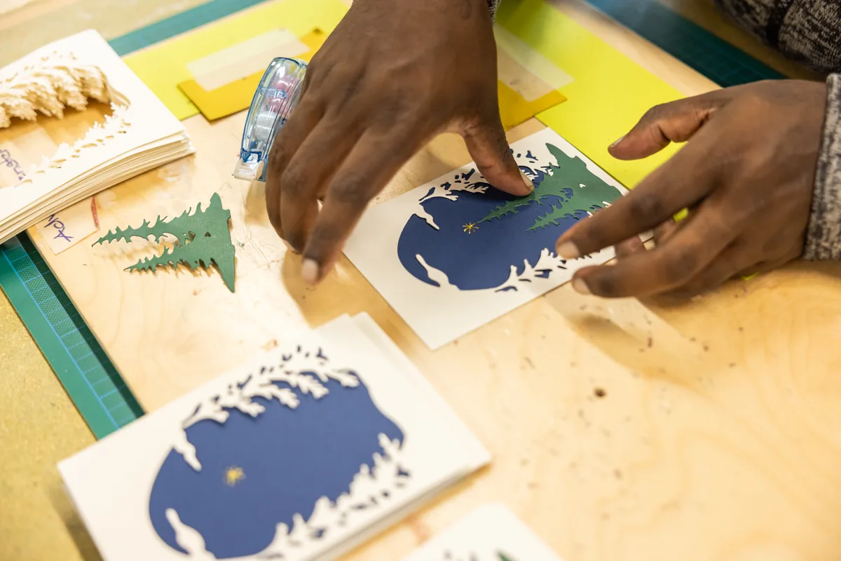 Auf dem Bild sind die Mitarbeiter des Werkheim-Betriebs Kunstvoll bei der Weihnachtskartenproduktion zu sehen.